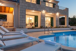 A modern house with a swimming pool, outdoor seating, and a well-lit entrance.