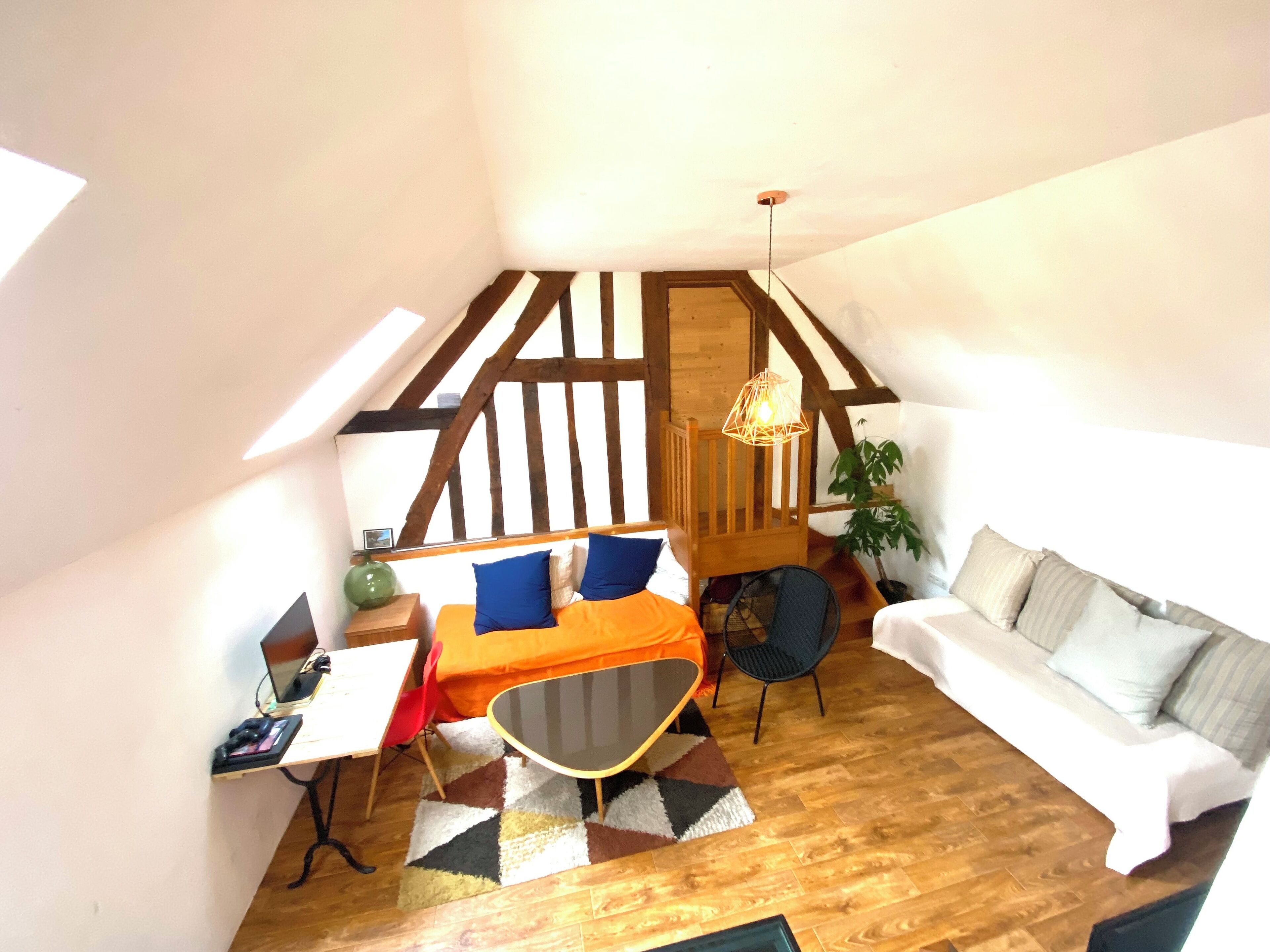Un espacio habitable compacto con techo estilo loft, una zona de comedor con mesa y sillas, un sofá y una lámpara colgante.
