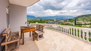 Un balcón con mesa y banco de madera, con vista a un pueblo y montañas.