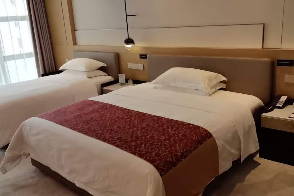 A hotel room with two beds, a nightstand with a phone, and a bedside table with a lamp.