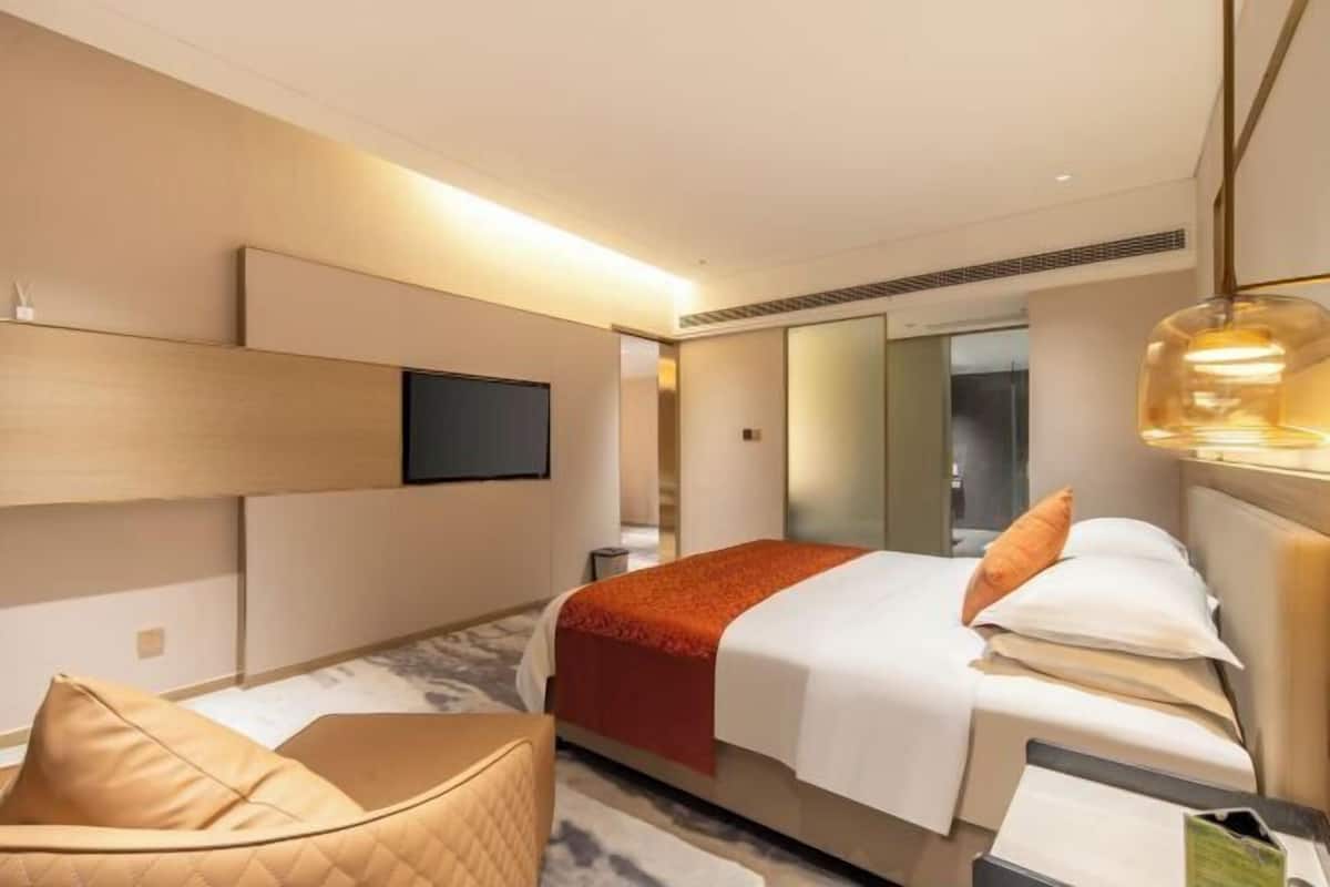 A modern hotel room with a bed, a seating area, a flat-screen TV, and a mirror.
