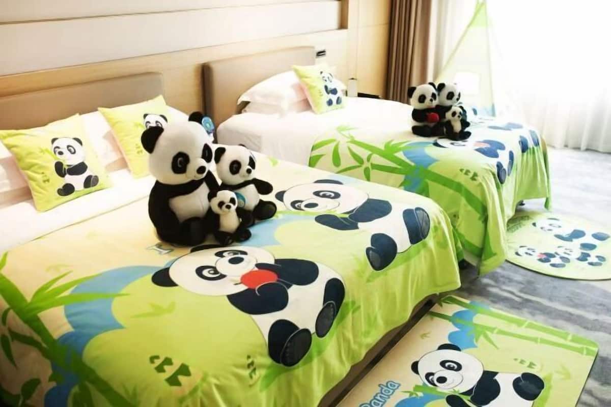 A hotel room with beds covered in green bedding featuring panda designs, and multiple panda plush toys on the beds.