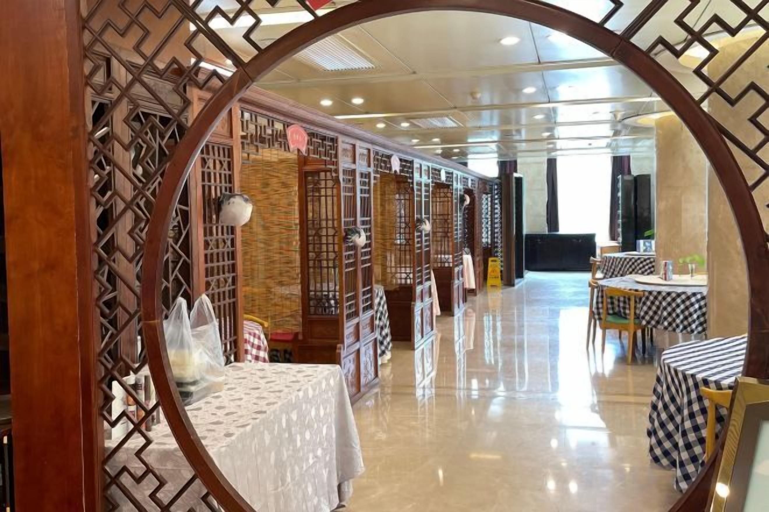 A modern interior with a reflective floor, wooden partitions, and tables with checkered tablecloths.