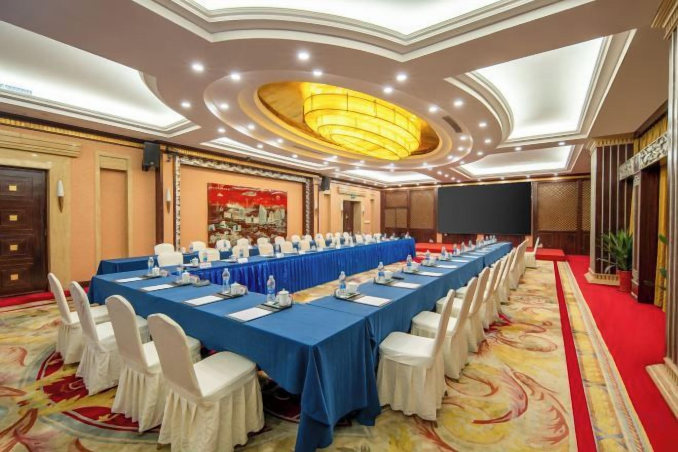 A conference room with a long table, white chairs, and a red carpet.