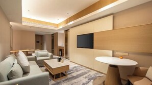 Ein modernes Hotelzimmer mit einer Sofagarnitur, einem Couchtisch, einem an der Wand befestigten Fernseher und einem runden Tisch.