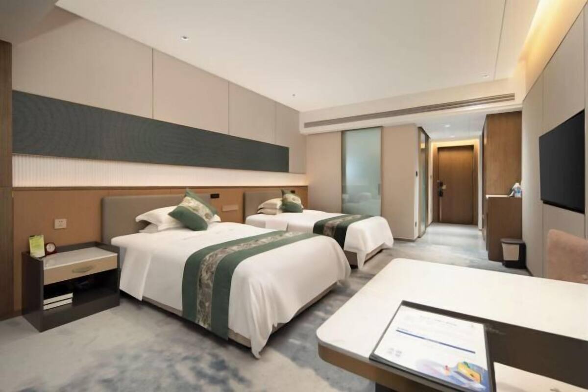 A hotel room with two beds, a desk, a TV, and a large mirror.
