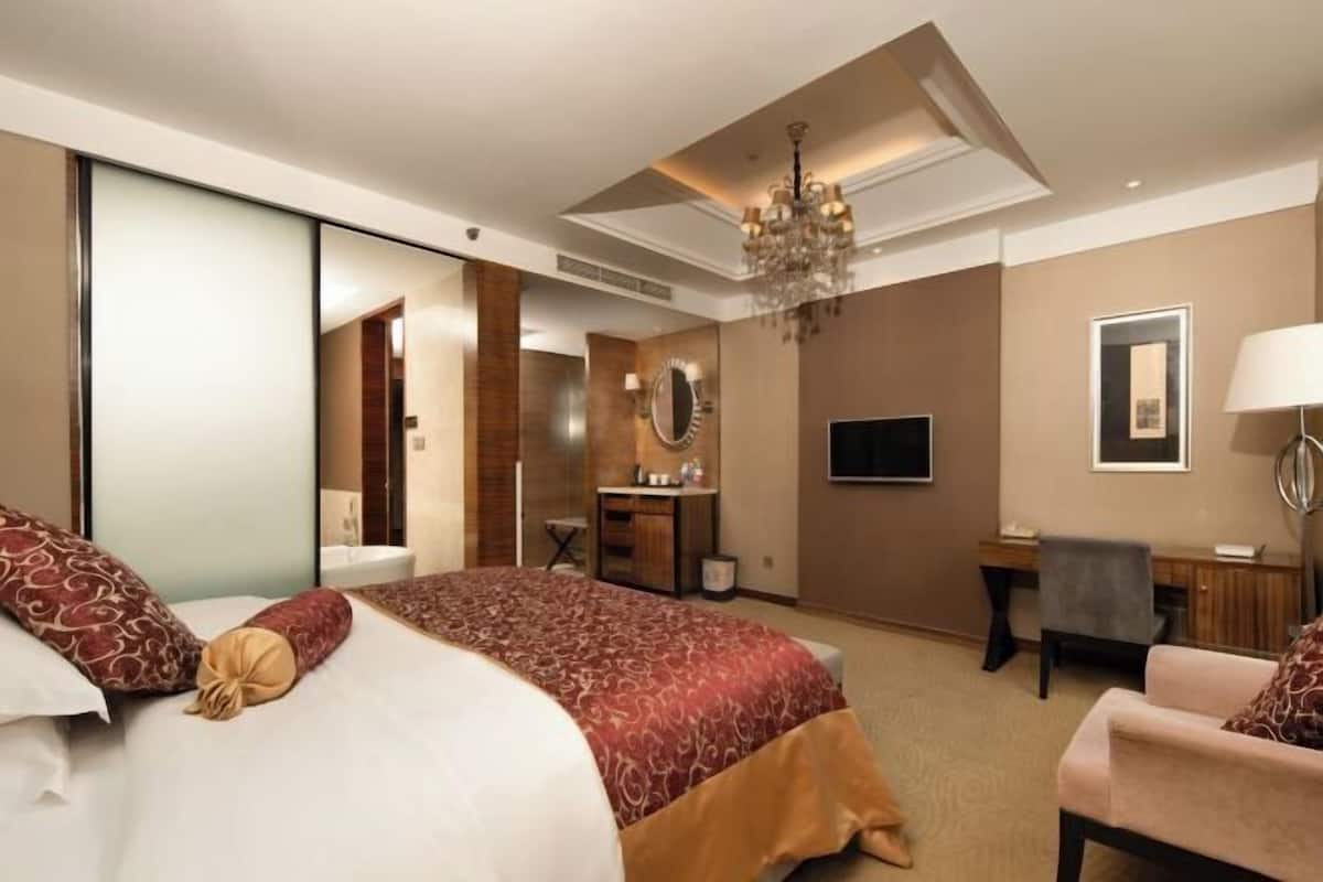 A hotel room with a large bed, a desk, a chair, a television, and a chandelier.