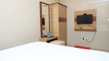 Una habitación de hotel moderna con una cama, un armario de madera, un espejo, un televisor montado en la pared y una pequeña mesa con una botella de agua.