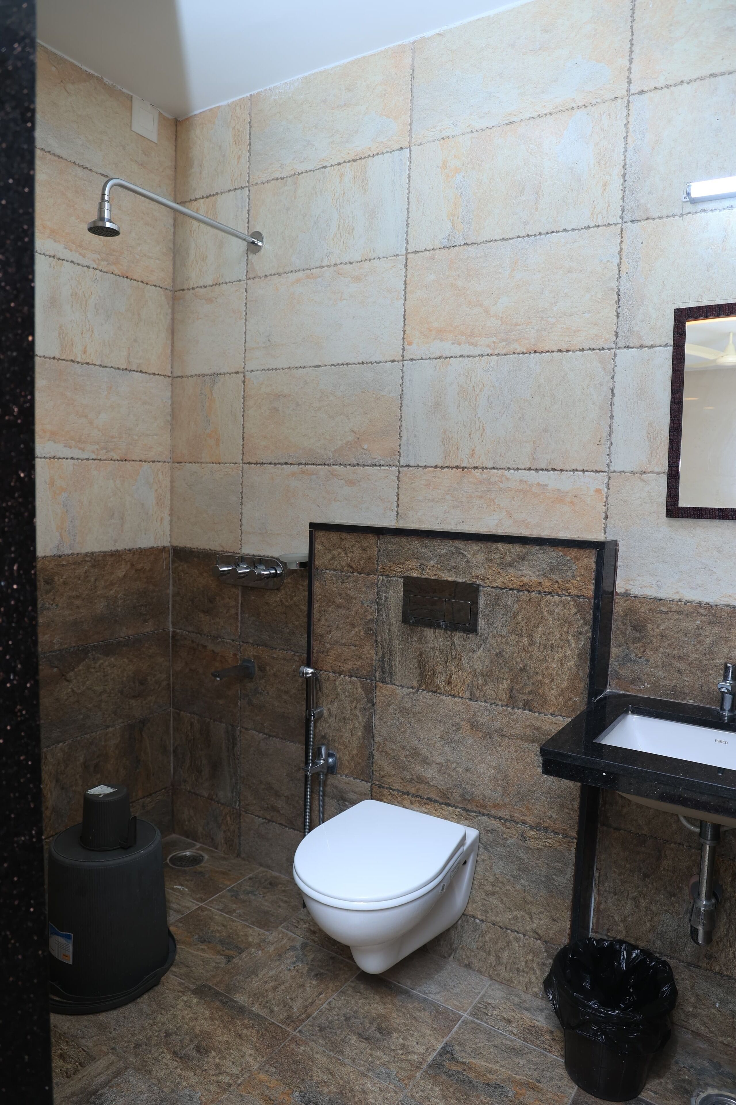 A bathroom with a shower, toilet, sink, and trash bin.