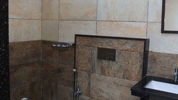 A bathroom with a shower, toilet, sink, and trash bin.