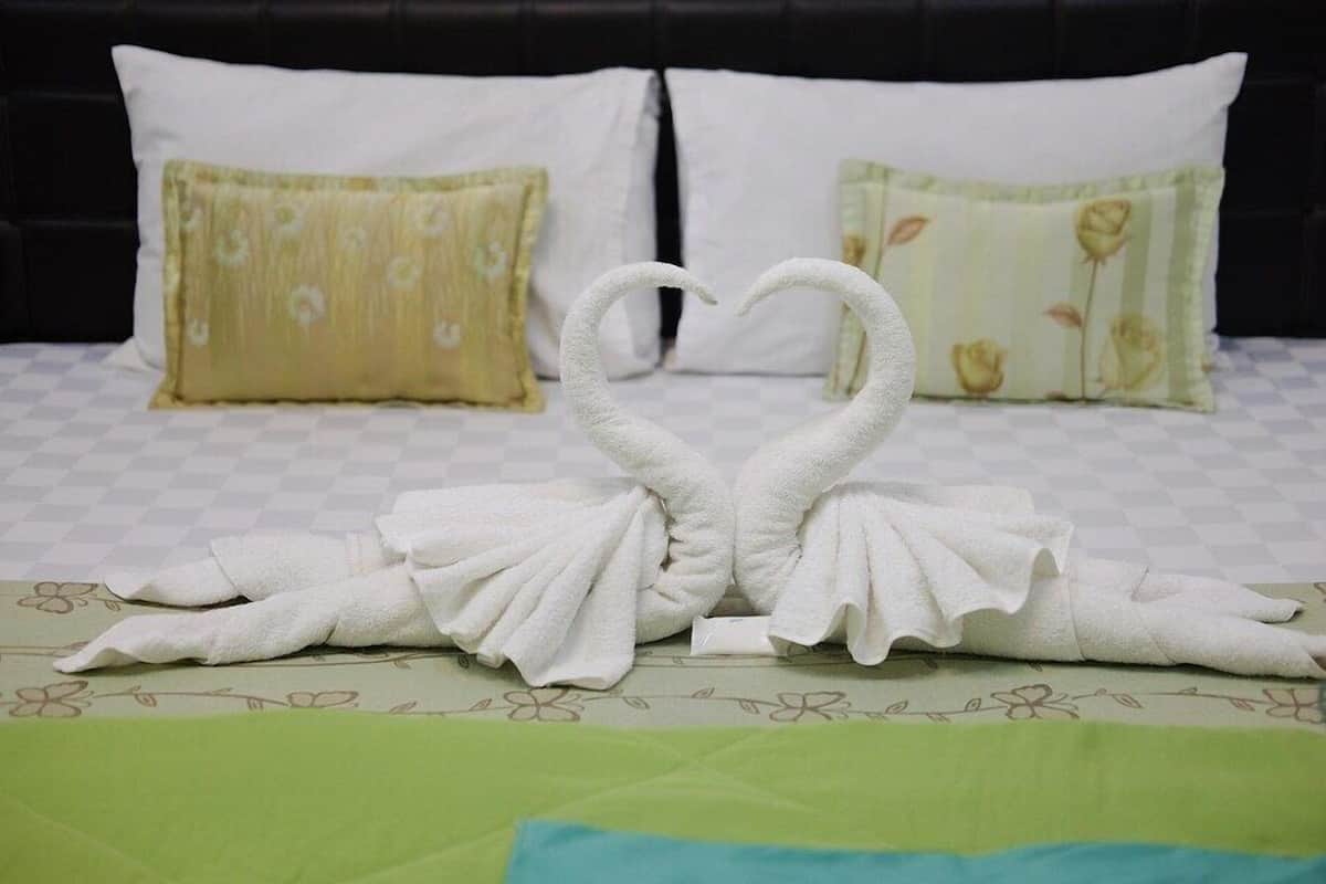 Un lit recouvert d’une couvre-lit à carreaux, deux oreillers ornés de motifs floraux et deux serviettes disposées en forme de cygnes.