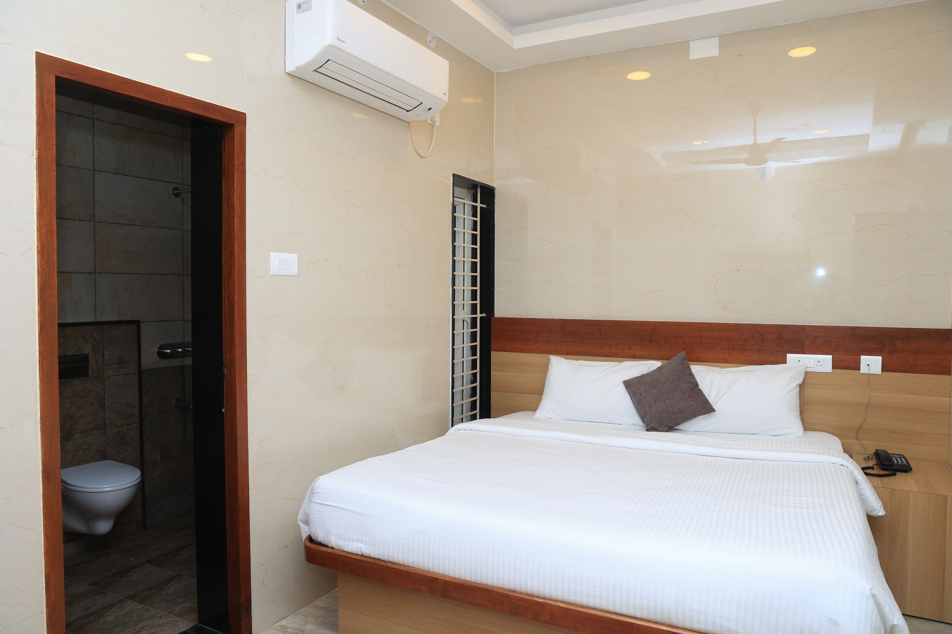 Une chambre d’hôtel avec un lit, une tête de lit en bois, une table de chevet avec un téléphone et un appareil de climatisation fixé au mur.