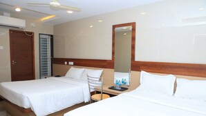 A hotel room with two beds, a wooden headboard, a mirror, a desk with a chair, and a ceiling fan. - TCS Residency (Kanchipuram)
