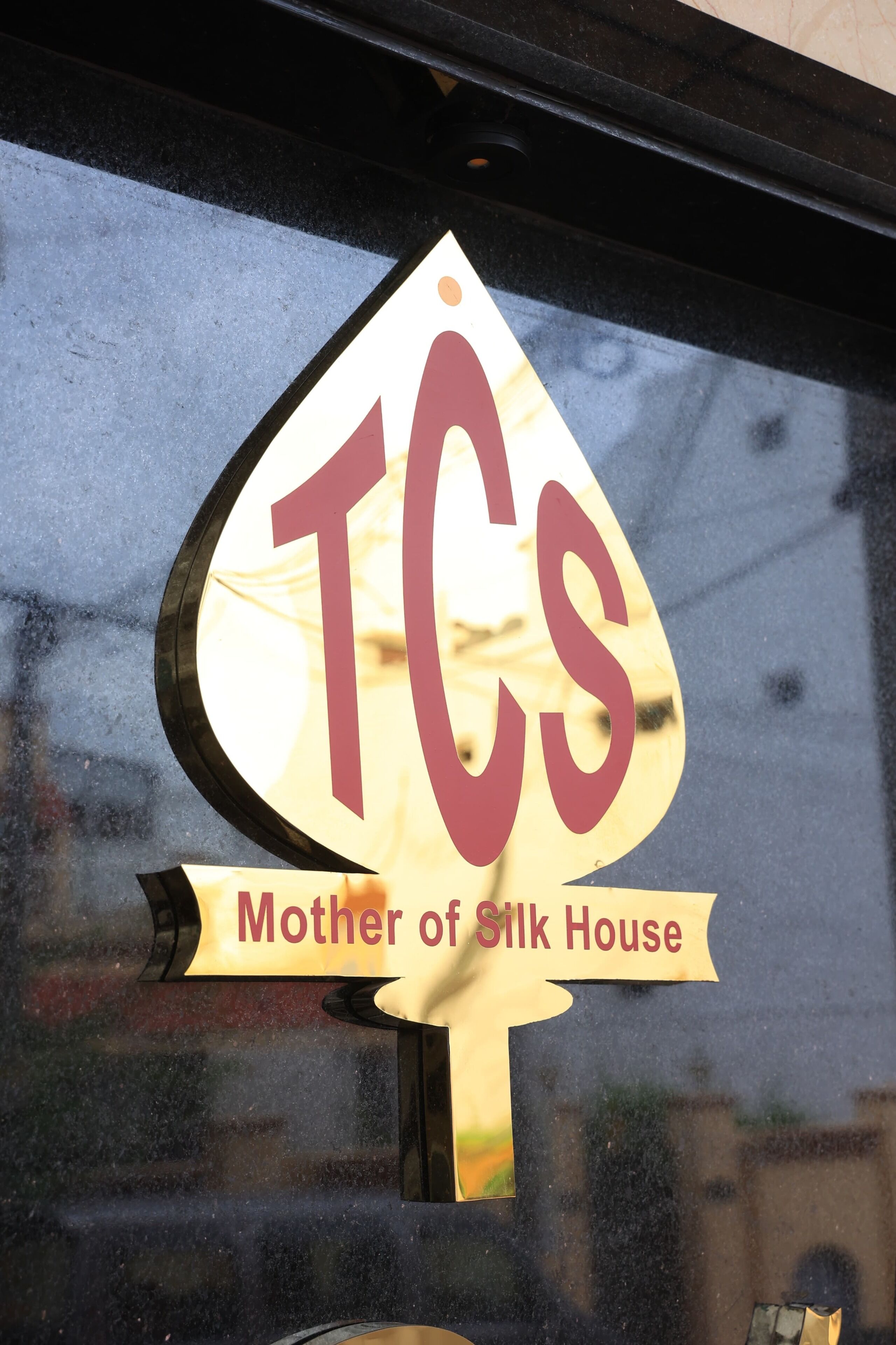 A sign with the text "TCS" and "Mother of Silk House" on a window.