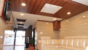 A lobby with a leather sofa, a glass coffee table, and a ceiling fan. - TCS Residency (Kanchipuram)