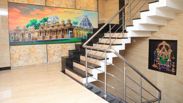 A modern interior with a marble wall, a staircase with metal railings, and a large painting of a temple. - TCS Residency (Kanchipuram)