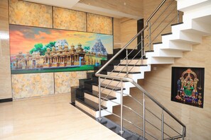 Un interior moderno con una pared de mármol, una escalera con barandillas metálicas y un cuadro grande de un templo.