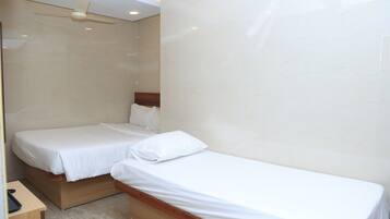 Habitación de hotel con dos camas individuales, cabecero de madera, un escritorio con teléfono y ventilador de techo.