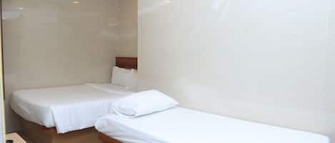 A hotel room with two single beds, a wooden headboard, a desk with a telephone, and a ceiling fan.