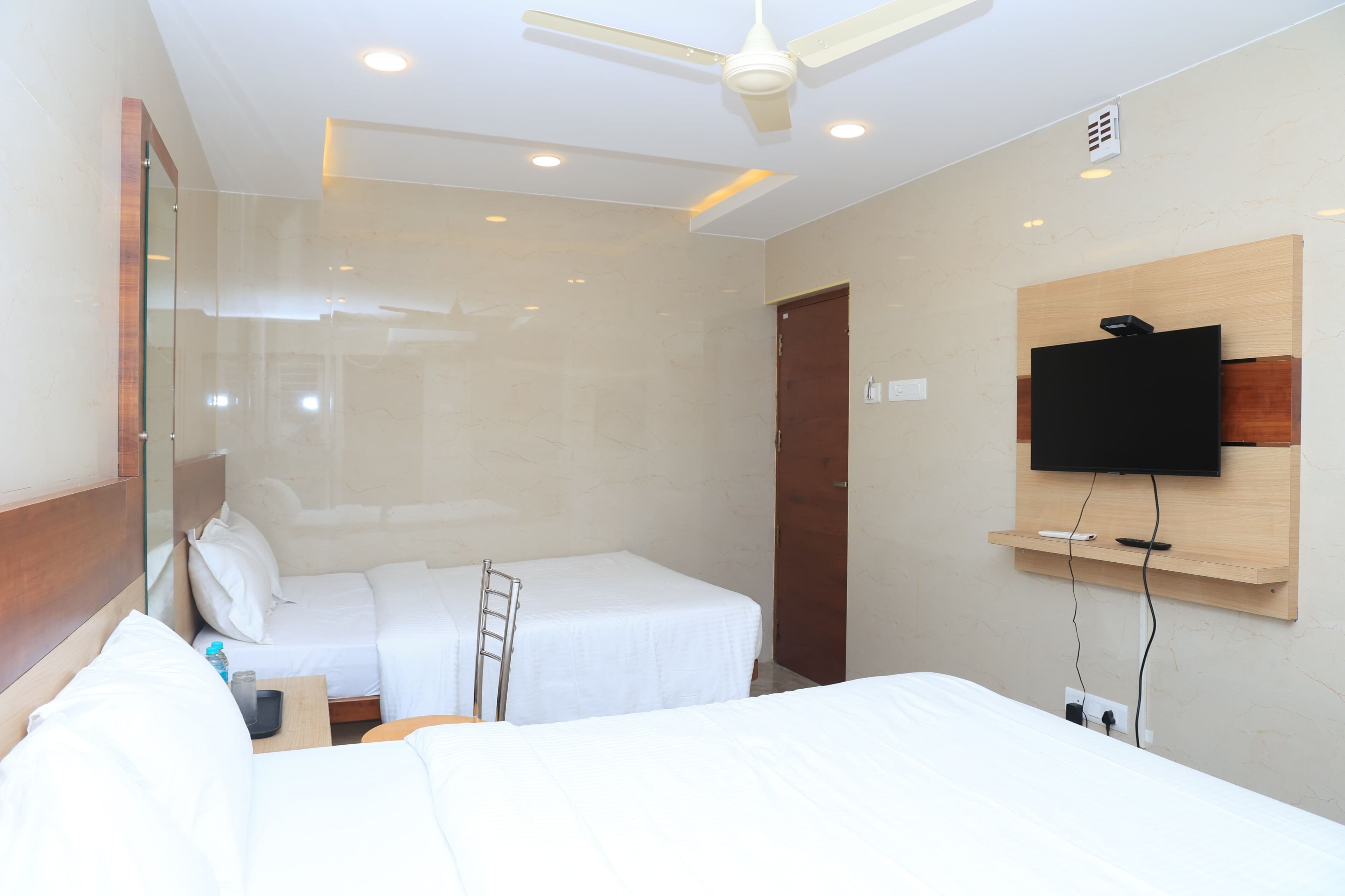 Una habitación de hotel con dos camas, un televisor montado en la pared y un ventilador de techo.