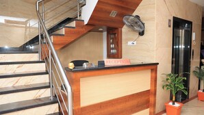 A reception desk with a marble staircase, a reception sign, an elevator, and a potted plant. - TCS Residency (Kanchipuram)