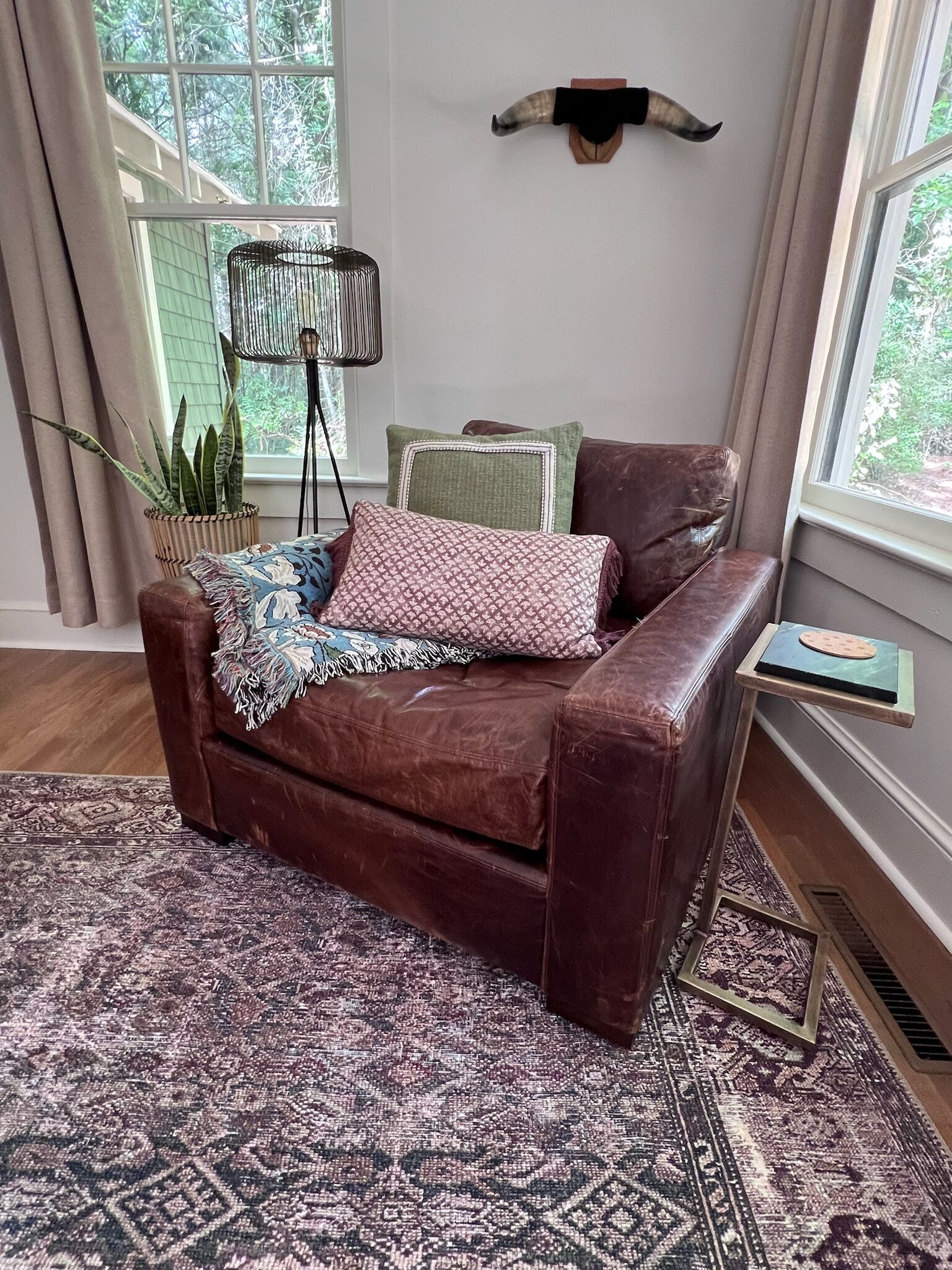 A brown leather sofa with a patterned throw blanket, a potted plant, and decorative pillows.