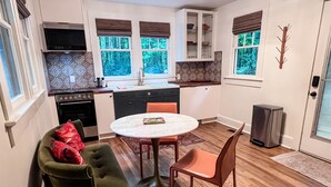 Una cocina compacta con comedor, que incluye una mesa redonda y dos sillas, horno empotrado y ventana con vistas a árboles.