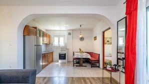 Una cocina moderna con armarios de madera, un refrigerador y un horno. Hay una zona de comedor con una mesa y sillas, y un sofá rojo.