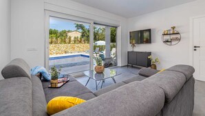 A modern living room with a grey sofa, a glass coffee table, and a TV mounted on the wall. - Villa KATHARINA with private pool (Žgaljići)