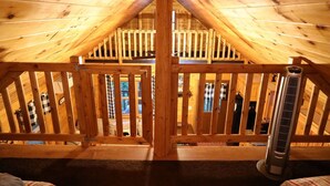 A wooden attic bedroom with a sloped ceiling, a central wooden staircase, and a standing heater. - Cozy Log Cabin, Sleeps 6, Pet Friendly! (Norway)