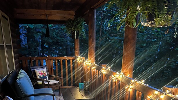A wooden deck with a bench and chairs, string lights, and a welcome mat. - Cozy Log Cabin, Sleeps 6, Pet Friendly! (Norway)