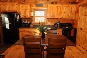 A wooden cabin kitchen with a dining table, chairs, a refrigerator, stove, and a window. - Cozy Log Cabin, Sleeps 6, Pet Friendly! (Norway)
