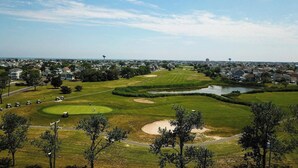 Un campo da golf con bunker di sabbia, uno stagno e edifici residenziali sullo sfondo.