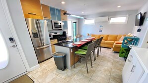 Una cucina moderna con elettrodomestici in acciaio inossidabile, una zona pranzo con tavolo e sedie, e un soggiorno con divano e TV.