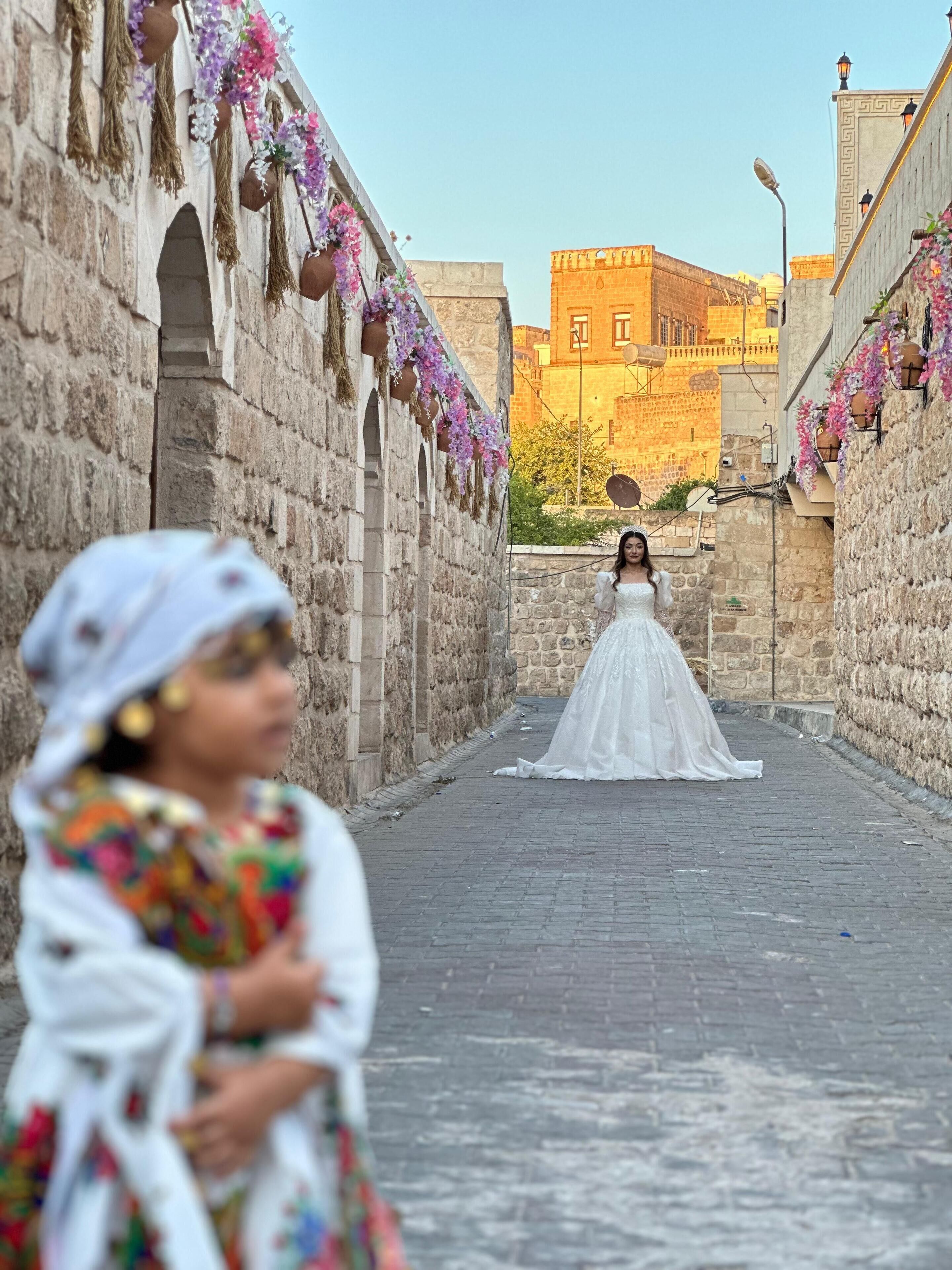 A narrow stone pathway with a person in a white dress and another in colorful attire.
