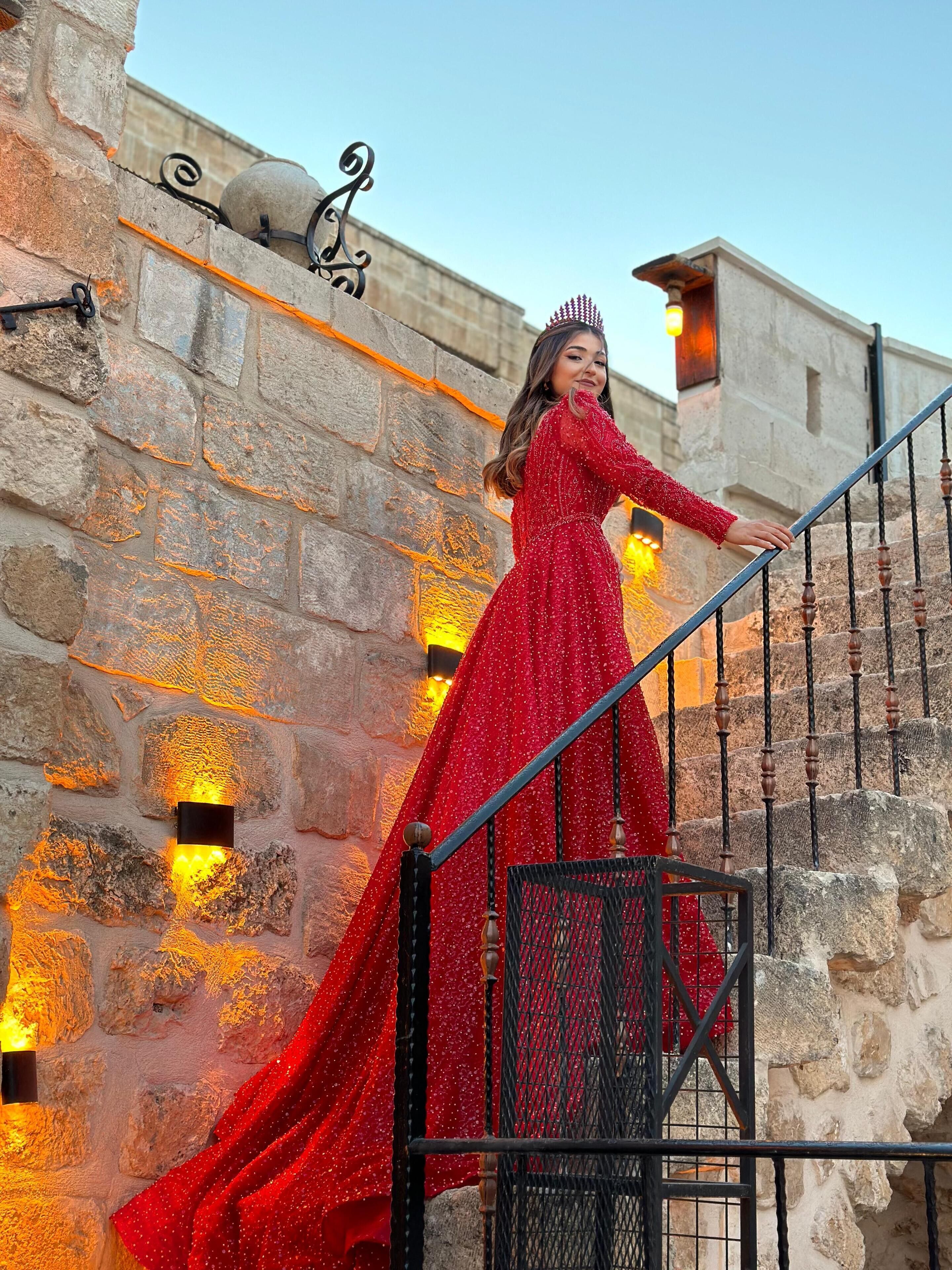 A person in a red dress descending a stone staircase with metal railings and decorative wall sconces.