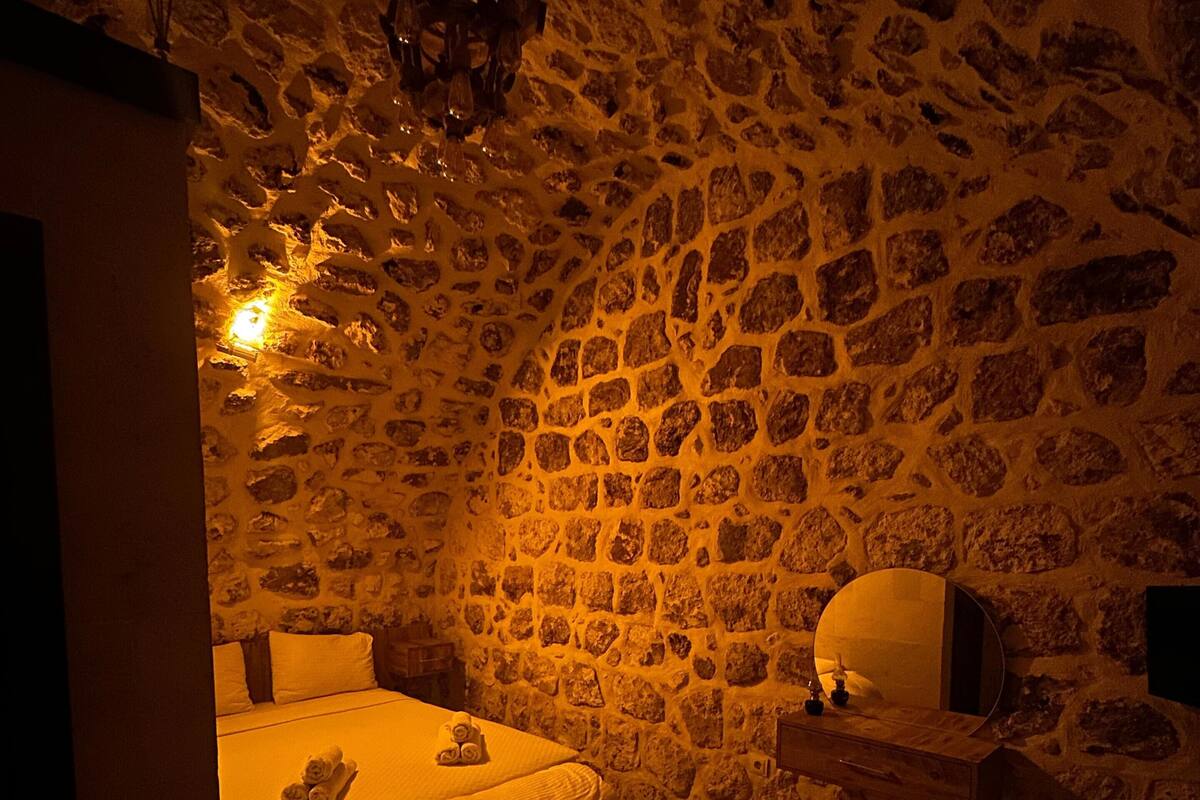 A cozy room with a stone wall, a bed with a white bedspread, and a small table with a lamp.