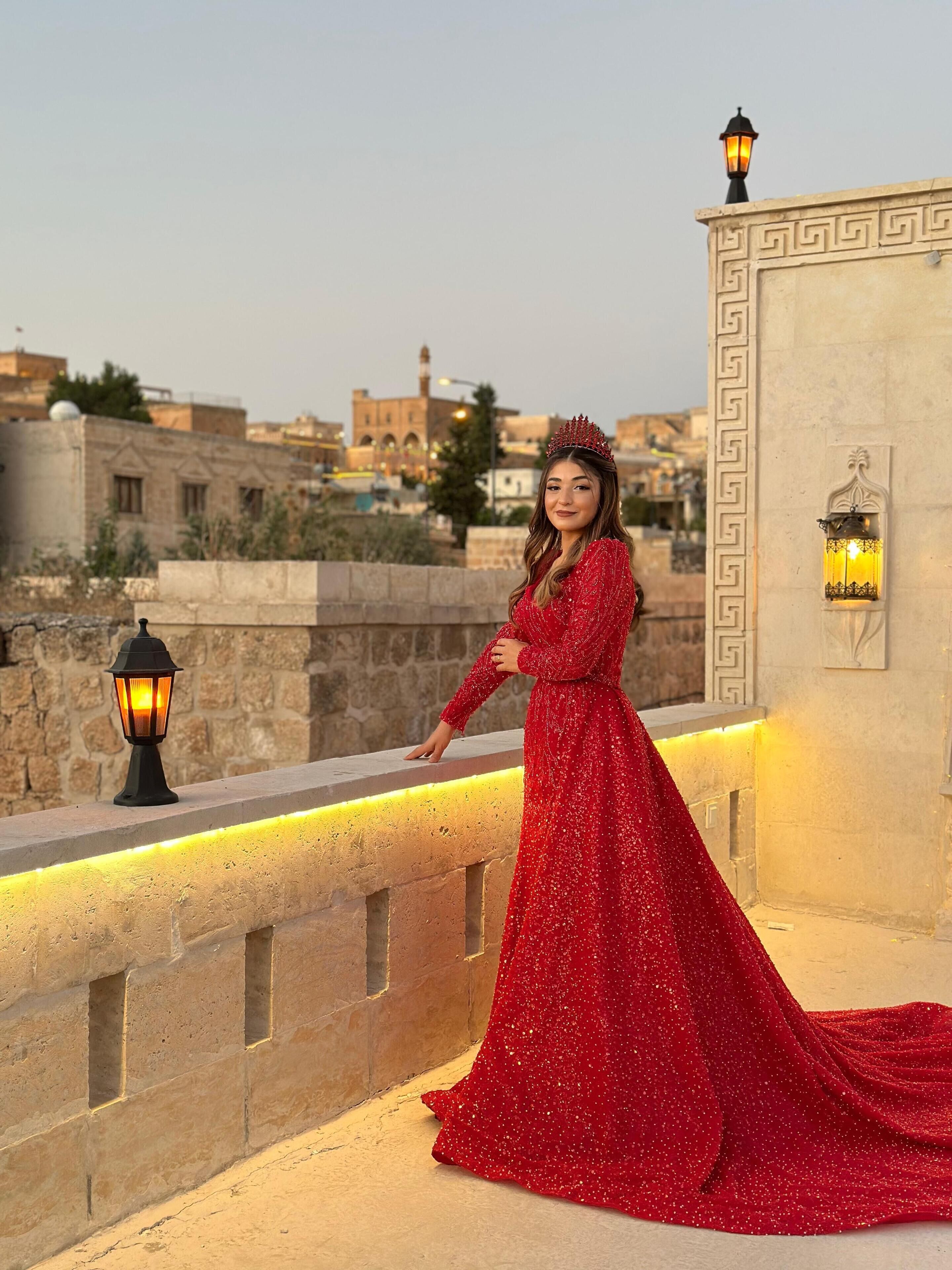 A woman in a red dress standing on a balcony with a cityscape in the background.