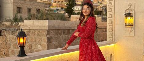 A woman in a red dress standing on a balcony with a cityscape in the background.