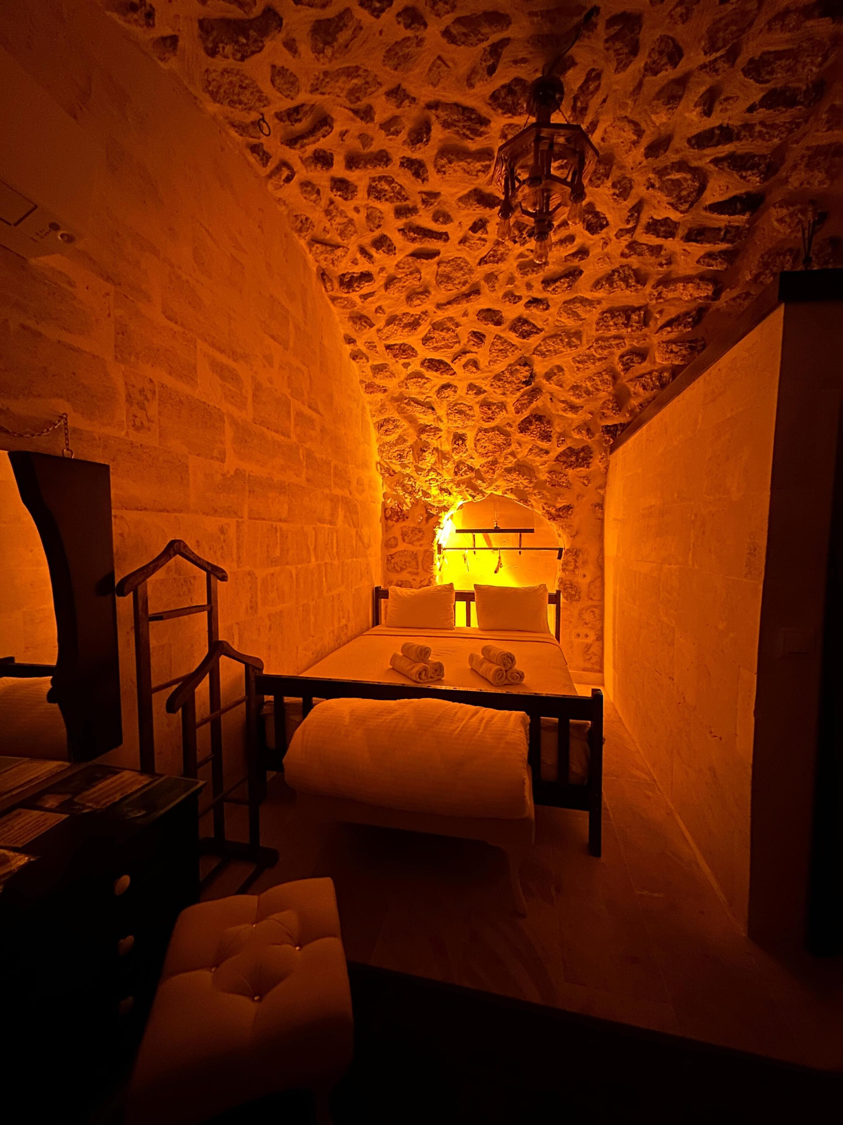 A cozy room with a stone ceiling, a bed with pillows, a wooden bench, and a small table.