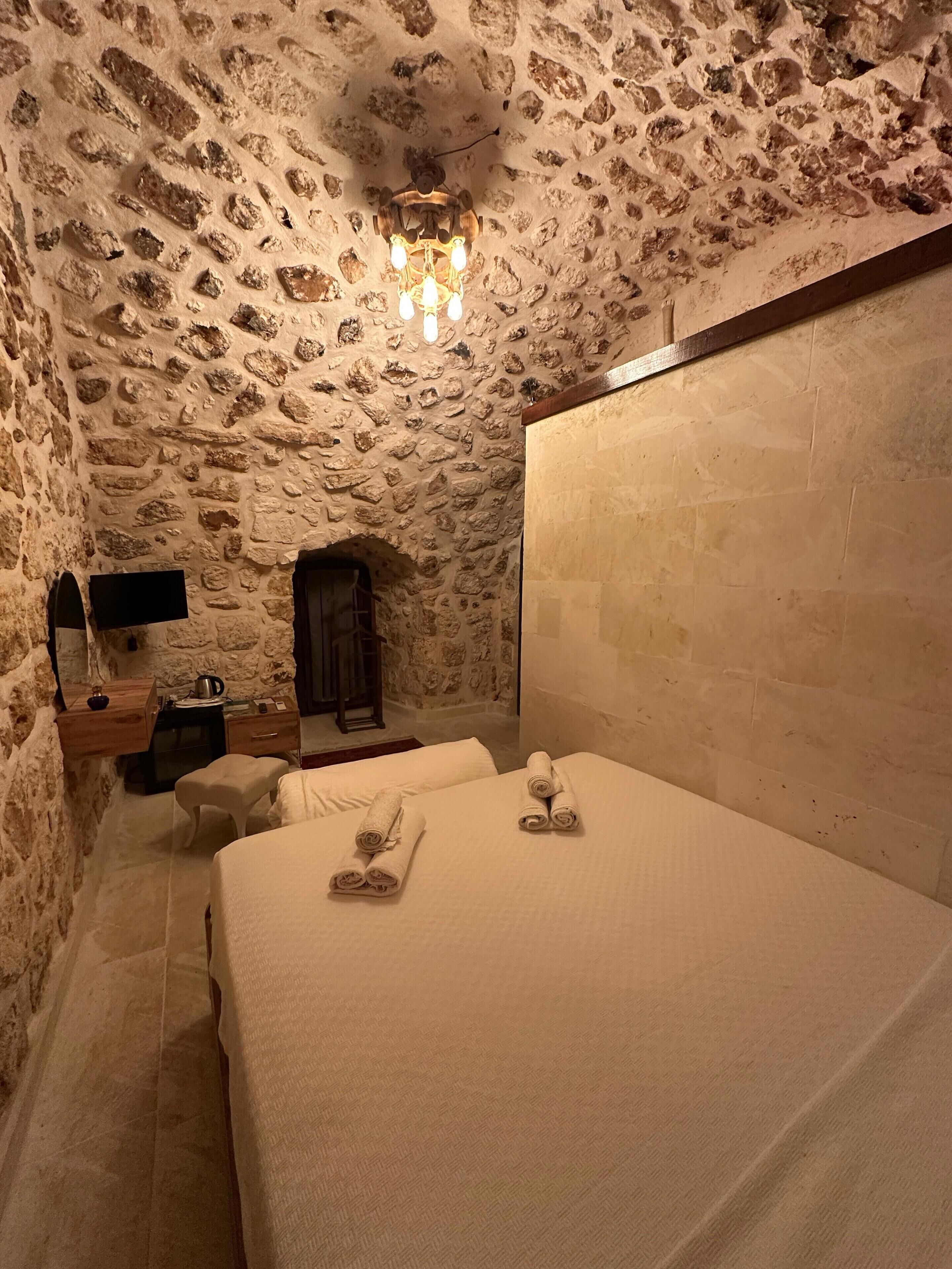 Una habitación de paredes de piedra con una cama, un escritorio y una mesita.