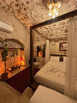 A stone-walled bedroom with a four-poster bed, a stone fireplace, and a potted plant. - Şahmeran Otel Cafe Restoran  (Midyat)