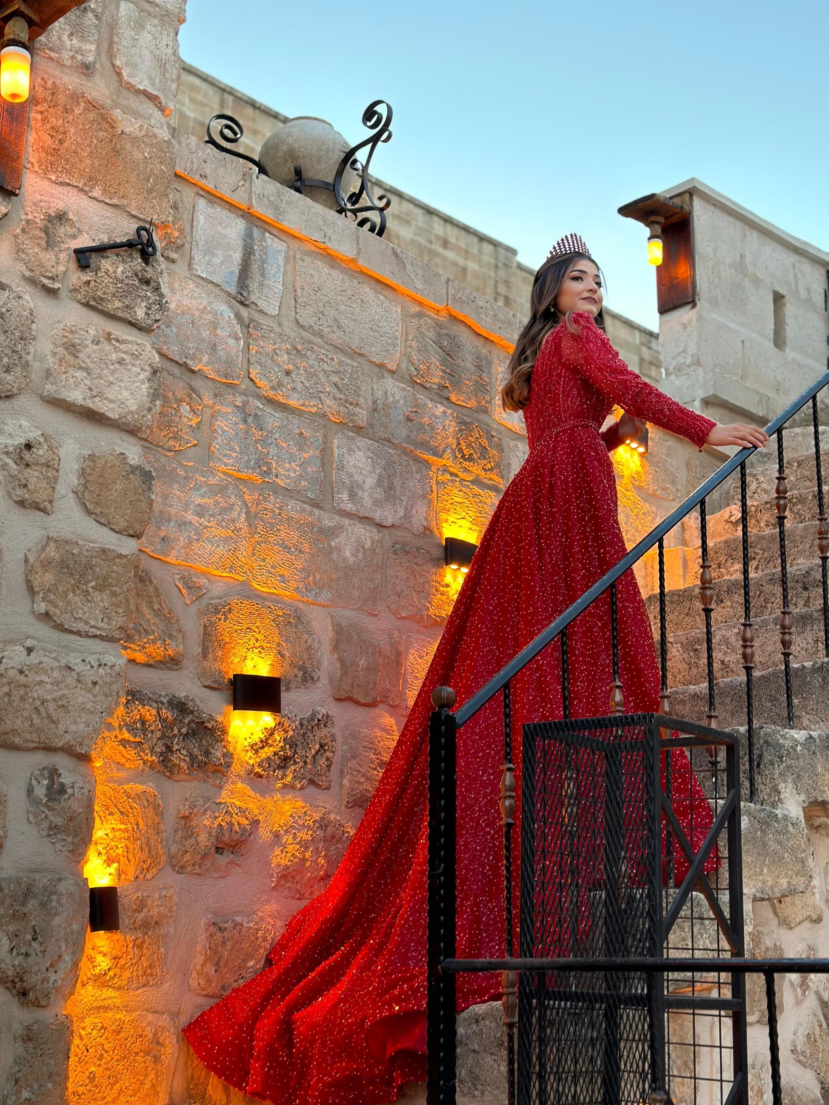 Una persona con un vestido rojo subiendo una escalera de piedra con barandillas metálicas y apliques decorativos.