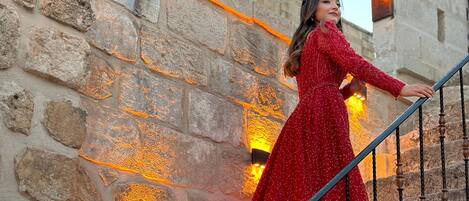 Una persona con un vestido rojo subiendo una escalera de piedra con barandillas metálicas y apliques decorativos.