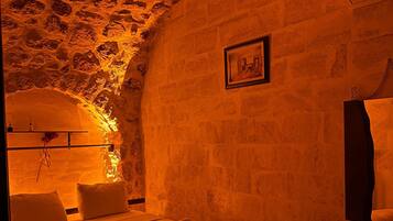 A room with a stone ceiling and walls, a bed with white linens, a bedside table, and a chair.