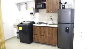 A compact kitchen with wooden cabinets, a stainless steel refrigerator, a microwave, and a gas stove. - Loft Entero Privado 25 Mts (Medellín)