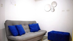 A grey sofa with blue cushions and a matching ottoman in a room with white walls and tiled flooring. - Loft Entero Privado 25 Mts (Medellín)
