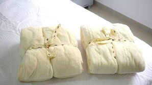Two neatly folded towels with floral patterns tied with ribbons on a bed with a textured white cover. - Loft Entero Privado 25 Mts (Medellín)