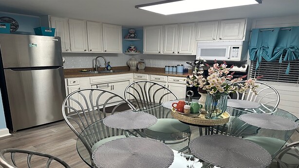 A modern kitchen with white cabinets, a stainless steel refrigerator, a microwave, and a dining area with a glass table and metal chairs.