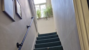 A staircase with a handrail, carpeted steps, and a window with plants. - A lovel one bedroom.  (London)